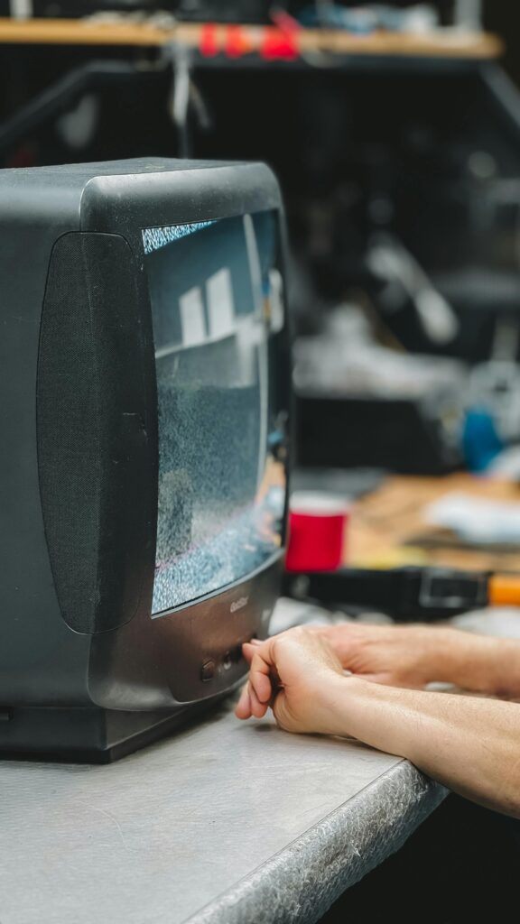 Close-up of hands adjusting a vintage CRT television displaying static in a workshop.