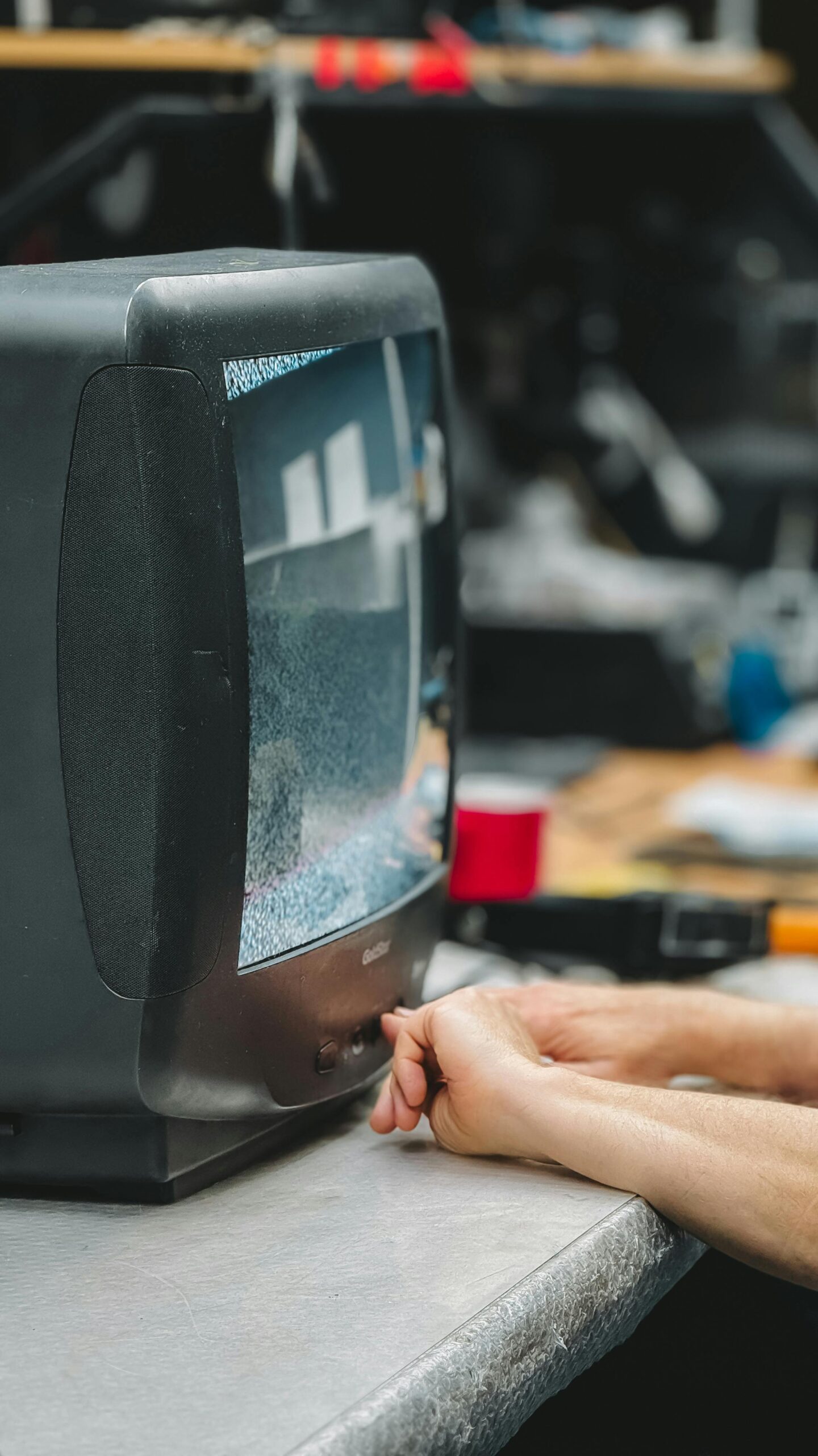 Close-up of hands adjusting a vintage CRT television displaying static in a workshop.
