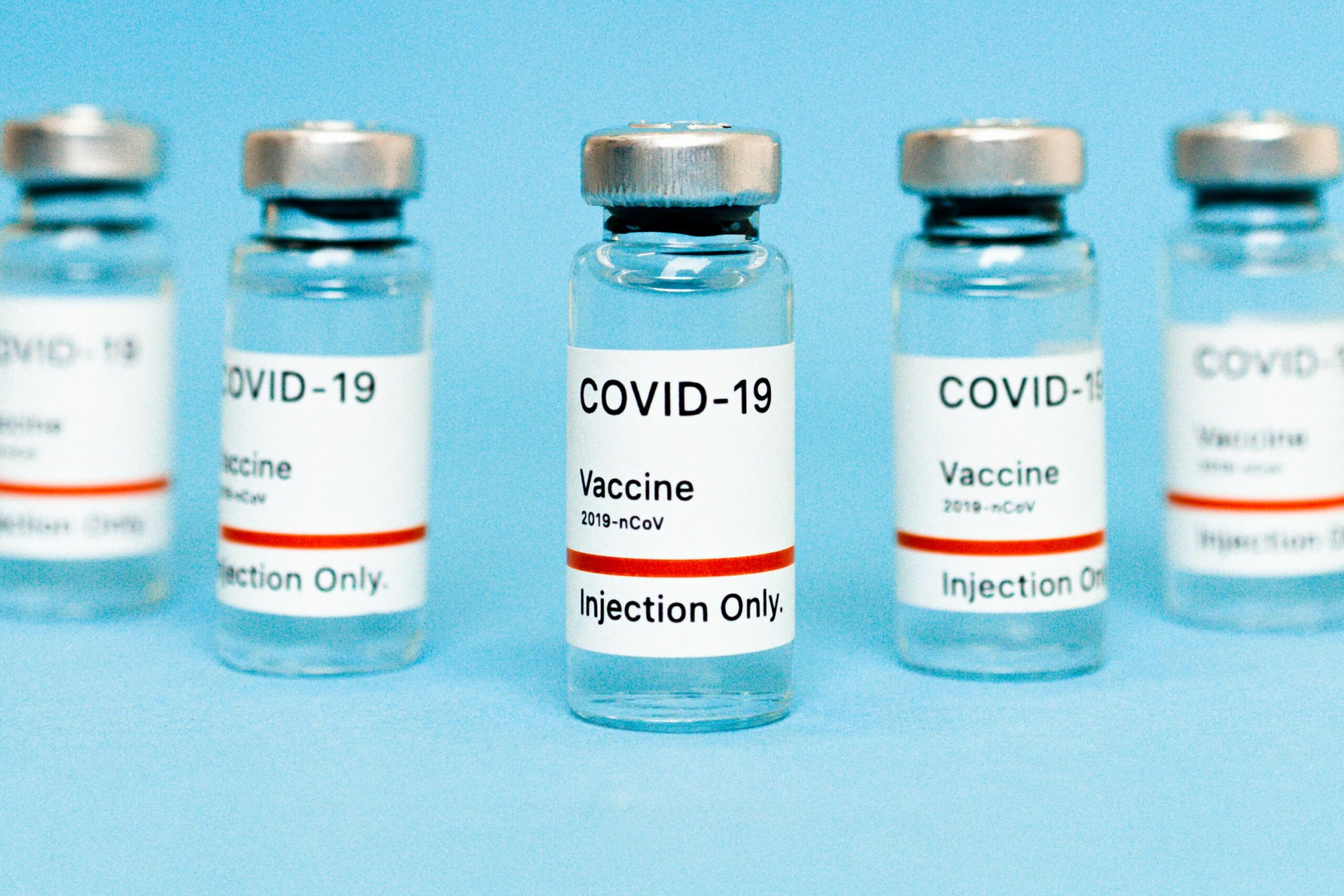 Close-up of COVID-19 vaccine vials labeled for injection on a blue background.
