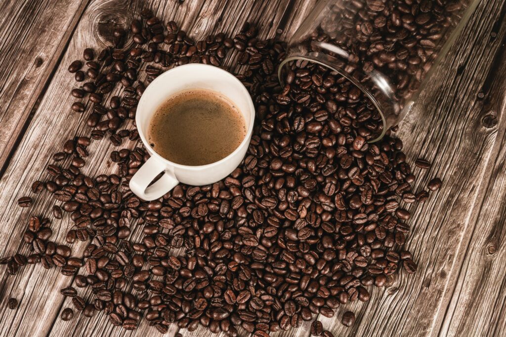 A coffee cup surrounded by spilled coffee beans on a rustic wooden table. Perfect for coffee lovers.