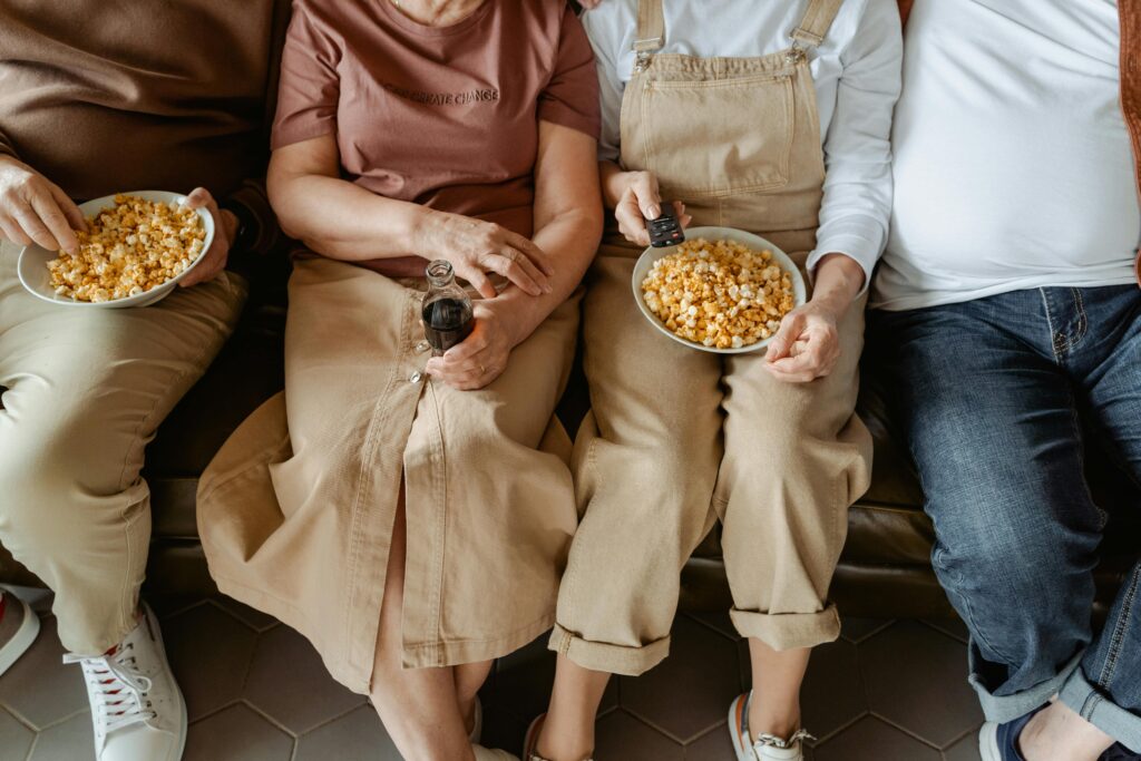 Elderly friends sharing popcorn and drinks during a cozy movie night at home.